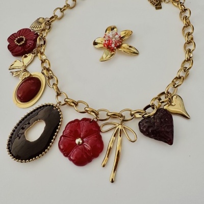 Colar com elos dourados e pendentes variados em flores vermelhas e formas douradas.