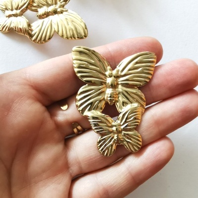 Dois ornamentos dourados em forma de borboleta na mão.