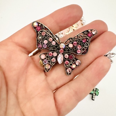 Broche borboleta com pedras rosas e lilás numa mão
