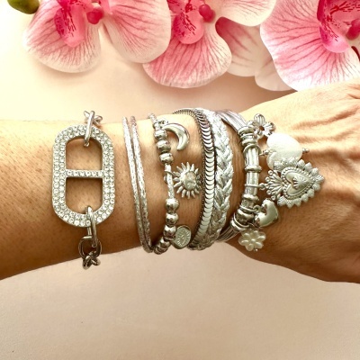 Braço com várias pulseiras prateadas e flores cor-de-rosa ao fundo