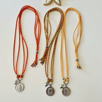 Três colares coloridos com pingentes redondos e uma flor decorativa sobre fundo branco.