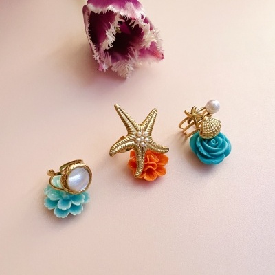 Três anéis dourados com decoração marinha e flores coloridas, ao lado de uma tulipa roxa.