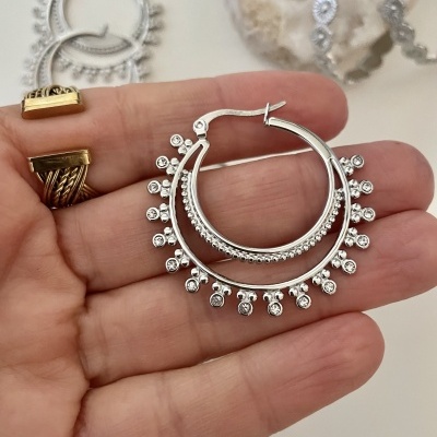 Brincos de argola prateados com detalhes circulares na mão