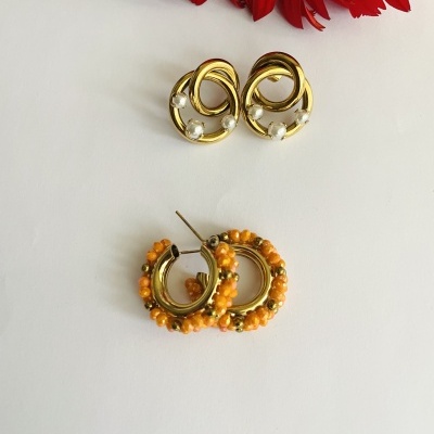 Dois pares de brincos dourados com pérolas e contas laranja em fundo branco com flores vermelhas