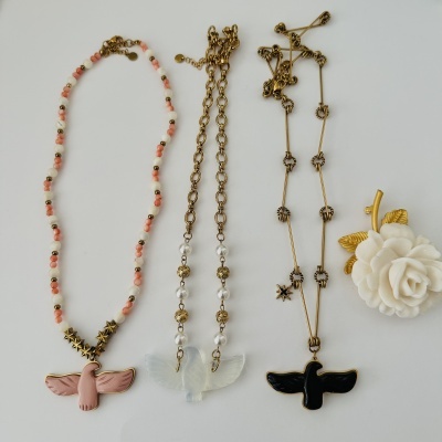 Colares com pendentes de pássaros rosa, branco e preto e um broche de flor branca e dourada