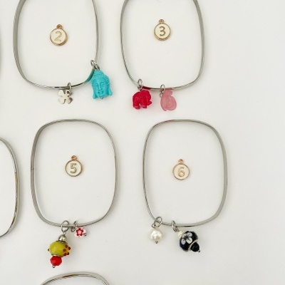 Quatro pulseiras quadradas de metal prateado com pendentes coloridos em fundo branco