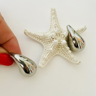 Brincos metálicos prateados em forma de gota sobre estrela-do-mar branca texturada.