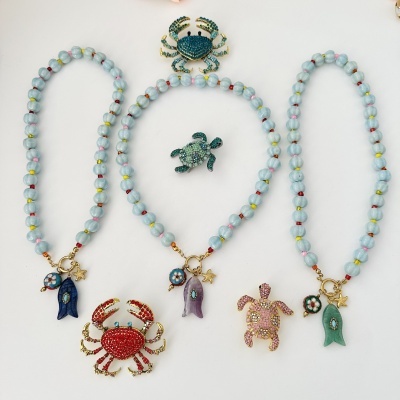Colares com contas azuis e pendentes coloridos com peixes e estrelas-do-mar, e broches de caranguejo e tartaruga coloridos