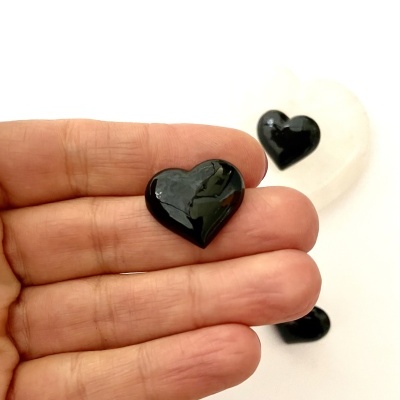 Três corações de pedra preta brilhante, um segurado por dedos