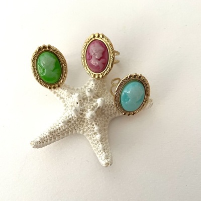 Anéis com pedras verdes, vermelhas e azuis em molduras douradas sobre estrela-do-mar branca