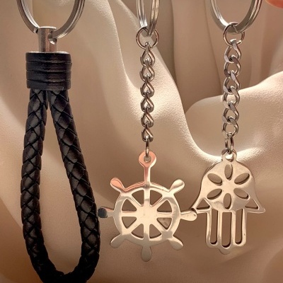 Três porta-chaves, dois metálicos com formas de leme e mão, um com tira trançada preta.