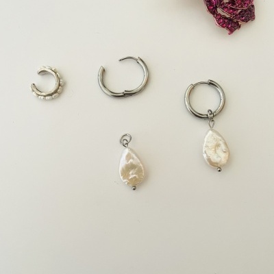 Três argolas metálicas prateadas com e sem pendente de pérola, sobre fundo branco, com flor decorativa de tecido