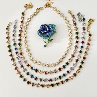 Conjunto de pulseiras com pedras coloridas e um broche de rosa azul com detalhes verdes