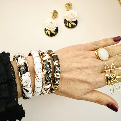 Pulseiras, brincos e anéis dourados com detalhes florais e pedras brancas em mão feminina.