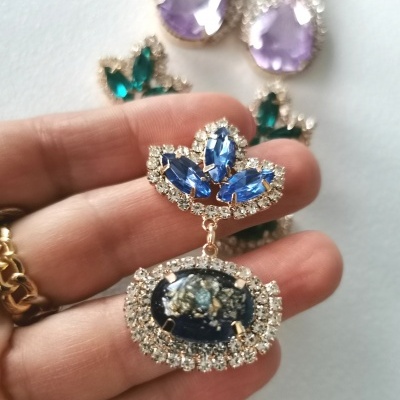 Brincos com pedras azuis e verdes decoradas com cristais pequenos em fundo branco