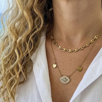 Colares dourados com pendentes usados sobre camisa branca com mar ao fundo