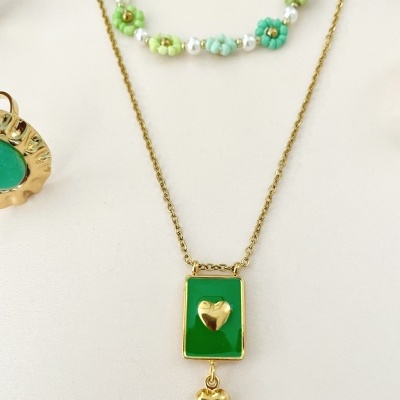 Colar dourado com pendente verde e corações dourados em fundo branco com anel e colar de contas ao fundo