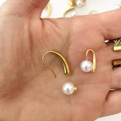 Brincos dourados com pérolas na mão, fundo branco com mais brincos