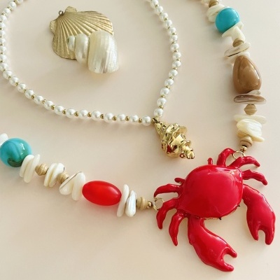 Colar com pendentes de concha dourada e caranguejo vermelho.