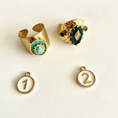 Dois anéis dourados com pedras verdes e dois pendentes brancos com números 1 e 2
