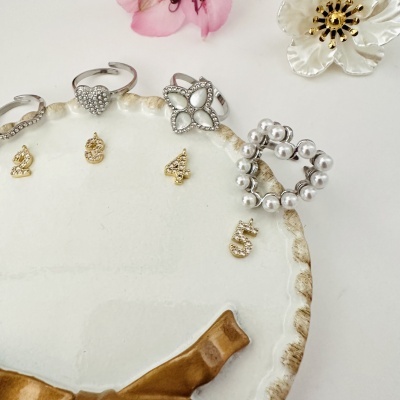 Anéis decorativos prateados com cristais e pérolas sobre prato branco decorativo com detalhes dourados.