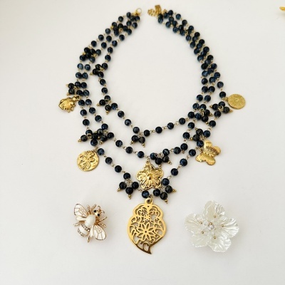 Colar triplo com contas pretas e pendentes dourados, com dois broches decorativos em branco e dourado