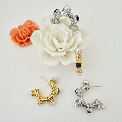 Brinco e anel em dourado e prateado com pérolas e pedras escuras sobre superfície branca com flores decorativas