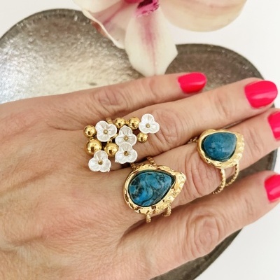 mão com anéis dourados e pedras azuis com flor-orquídea ao fundo