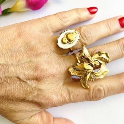 Mão com anéis dourados florais e unhas vermelhas, fundo branco com flores