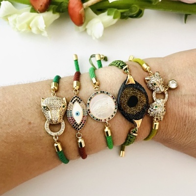 Pulseiras com pendentes dourados e cordão em verde e vermelho na mão.