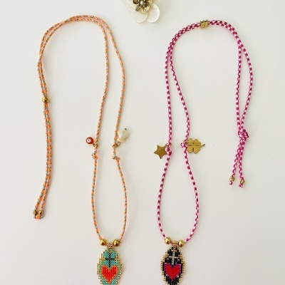 Dois colares com pendentes coloridos e suporte floral branco ao fundo