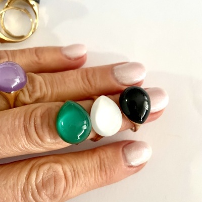 Mãos a mostrar anéis com pedras coloridas em fundo branco