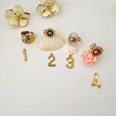 Anel dourado com botão azul e detalhes florais sobre conchas, flores e pendentes numéricos
