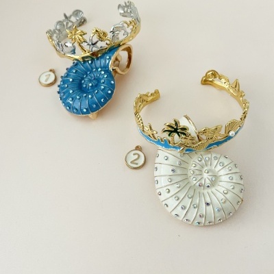 Dois anéis decorativos com conchas azul e branca e detalhes dourados e prateados