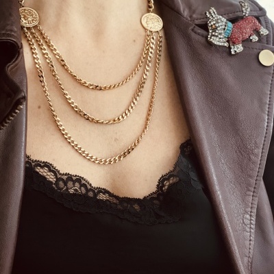 Colares dourados em pescoço com camisola preta de renda e casaco de couro castanho com broche de coelho