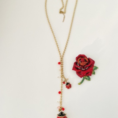 Colar dourado com pendentes de joaninhas e aplicação bordada de rosa