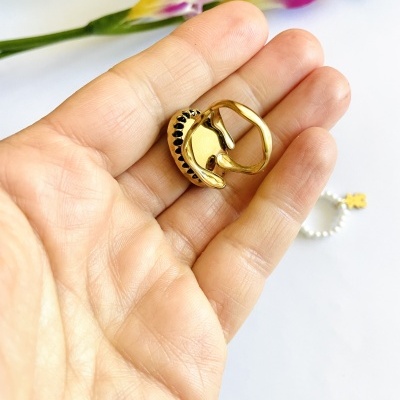 Anel dourado com detalhes pretos na mão com flores ao fundo