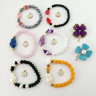 Seis pulseiras coloridas numeradas e dois alfinetes de flores sobre fundo branco.