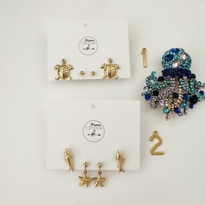 Brincos em suporte branco com logótipo Maria COTOVIA e joia em design de polvo azul com pedras