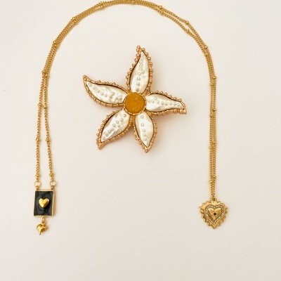 Colar dourado com pingentes preto e dourado ao lado de broche flor branca e amarelo