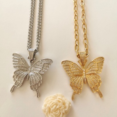 Dois pendentes de borboleta em colares prateado e dourado com detalhe de flor branca