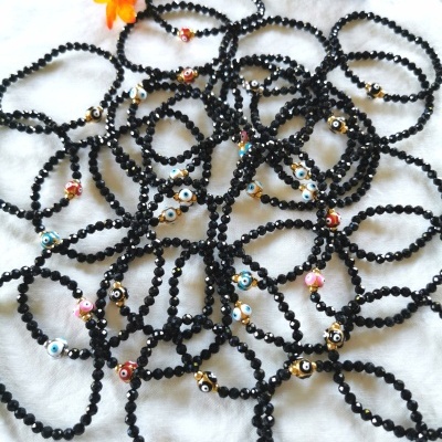 Colares ou pulseiras de contas pretas com contas coloridas em forma de olho sobre pano branco com flores.