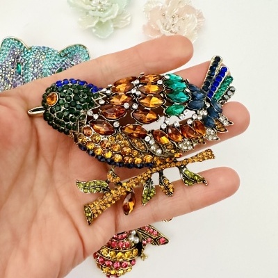 Broche pássaro com pedras coloridas na mão sobre fundo branco