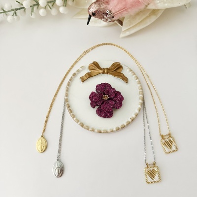 Colares e broche decorativos em suporte branco com laço dourado.