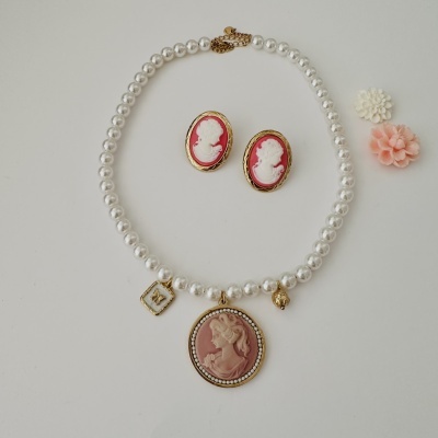 Colar de pérolas com pendente rosa e brincos camafeus rosas sobre fundo branco