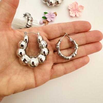 Par de brincos argola prateados com textura arredondada e bambu numa mão