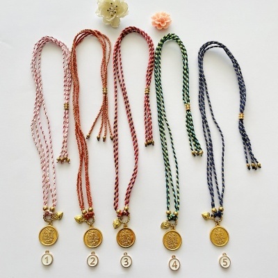 Cinco colares com cordões trançados coloridos e pendentes dourados numerados de 1 a 5