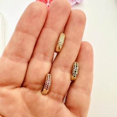 Três brincos dourados com pedras coloridas em mão aberta