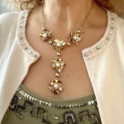 Colar dourado com flores e pérolas usado com casaco branco e top verde decorado