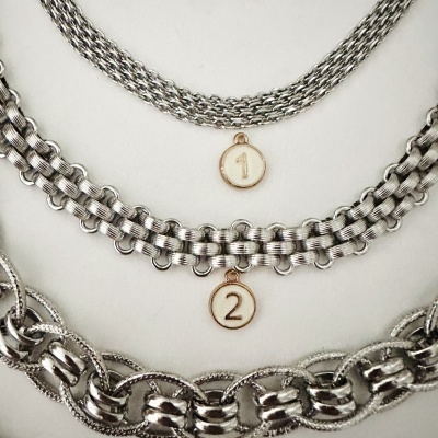 Três pulseiras metálicas prateadas com medalhões numerados 1 e 2